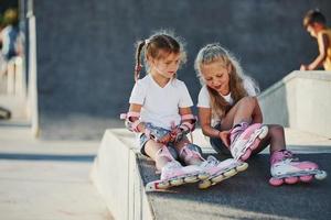 Having a rest. On the ramp for extreme sports. Two little girls with roller skates outdoors have fun photo