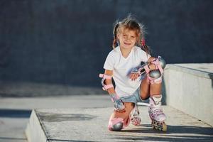 Cute little girl with roller skates outdoors sits on the ramp for extreme sports photo