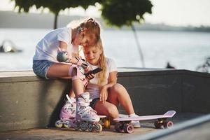 Talking with each other. On the ramp for extreme sports. Two little girls with roller skates outdoors have fun photo