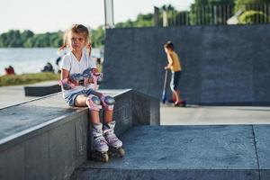 Cute little girl with roller skates outdoors sits on the ramp for extreme sports photo