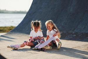 relajarse y conversar. en la rampa para los deportes extremos. dos niñas pequeñas con patines al aire libre se divierten foto