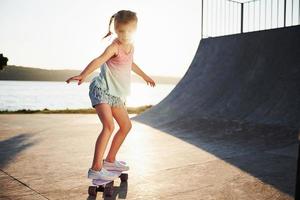 First attempts. Sunny day. Kid have fun with skate at the ramp. Cheerful little girl photo