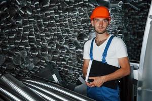 Full stack of ventilation pipes. Man in uniform works on the production. Industrial modern technology photo