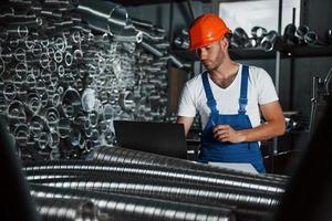 Brand new ventilation pipes. Man in uniform works on the production. Industrial modern technology photo