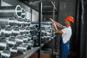 Takes one of the ventilation pipes. Man in uniform works on the production. Industrial modern technology photo