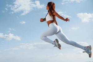 Up in the sky. Female runner in white sportive clothes doing fitness photo