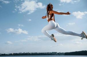 Up in the sky. Female runner in white sportive clothes doing fitness photo