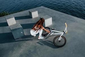 Near the bike. Fitness woman having a rest near the lake at daytime. Beautiful sunlight photo