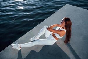 Doing abs. Shot of sportive woman doing fitness exercises near the lake at daytime photo