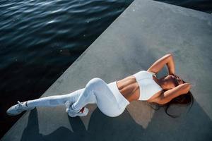 Top view. Shot of sportive woman doing fitness exercises near the lake at daytime photo