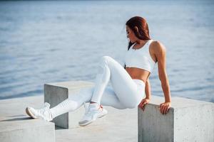 Shot of sportive woman doing fitness exercises near the lake at daytime photo