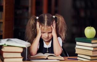 Tired of reading. Cute little girl with pigtails is in the library. Apple on the books photo