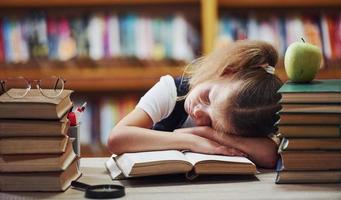 Sleeping on the table. Cute little girl with pigtails is in the library. Apple on the books photo