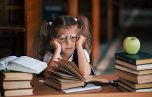 Bored and tired. Cute little girl with pigtails is in the library. Apple on the books photo