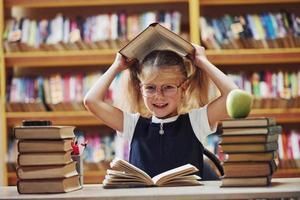 Playful mood. Cute little girl with pigtails is in the library. Apple on the books photo