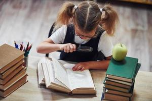 Holds magnifier. Cute little girl with pigtails is in the library. Apple on the books photo