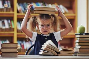 estado de ánimo juguetón. linda niña con coletas está en la biblioteca. manzana en los libros foto