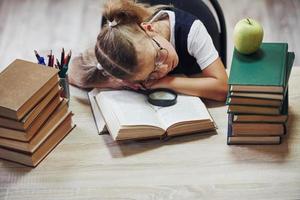 durmiendo sobre la mesa. linda niña con coletas está en la biblioteca. manzana en los libros foto