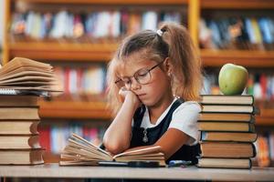 Cute little girl with pigtails is in the library. Apple on the books photo