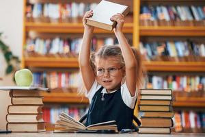 Cute little girl with pigtails is in the library. Apple on the books photo