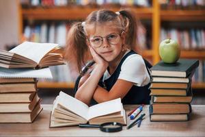 linda niña con coletas está en la biblioteca. manzana en los libros foto