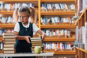 linda niña con coletas está en la biblioteca. manzana en los libros foto