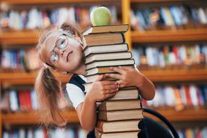 linda niña con coletas está en la biblioteca. manzana en los libros foto