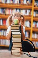 Cute little girl with pigtails is in the library. Apple on the books photo