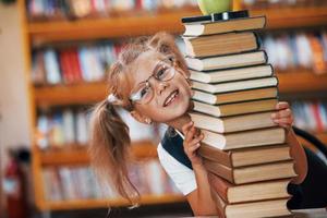 Cute little girl with pigtails is in the library. Apple on the books photo