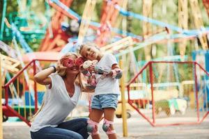 Eating donuts. Cheerful little girl on roller skates and her mother have a good time in the park together near attractions photo