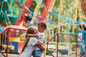 Embracing each other. Cheerful little girl her mother have a good time in the park together near attractions photo