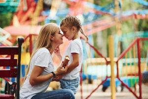 Eating ice cream. Cheerful little girl her mother have a good time in the park together near attractions photo