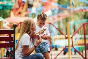Eating ice cream. Cheerful little girl her mother have a good time in the park together near attractions photo