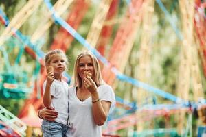 Comiendo helado. niña alegre su madre se divierten juntos en el parque cerca de las atracciones foto