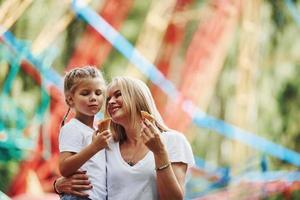 Eating ice cream. Cheerful little girl her mother have a good time in the park together near attractions photo