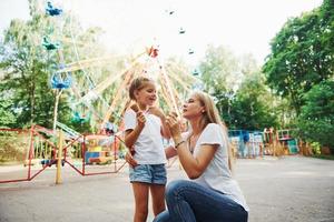 Eating ice cream. Cheerful little girl her mother have a good time in the park together near attractions photo