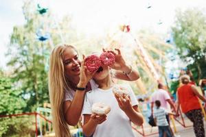 Having fun with donuts. Cheerful little girl her mother have a good time in the park together near attractions photo