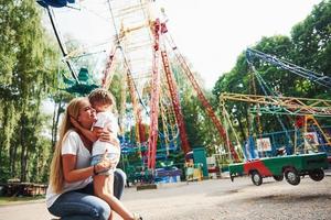 da abrazos. niña alegre su madre se divierten juntos en el parque cerca de las atracciones foto