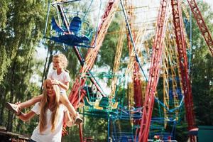 niña alegre su madre se divierten juntos en el parque cerca de las atracciones foto