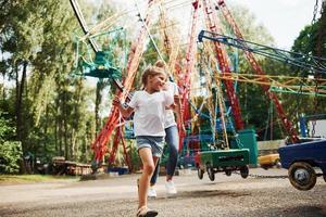 Running and playing. Cheerful little girl her mother have a good time in the park together near attractions photo