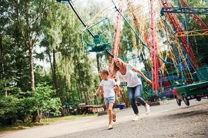 corriendo y jugando. niña alegre su madre se divierten juntos en el parque cerca de las atracciones foto