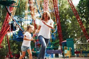 corriendo y jugando. niña alegre su madre se divierten juntos en el parque cerca de las atracciones foto