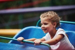 retrato de una niña feliz diviértete en una montaña rusa en el parque durante el día foto