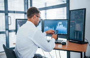 Searching information. Young businessman in formal clothes is in office with multiple screens. Conception of exchange and money photo