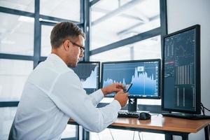 Searching information. Young businessman in formal clothes is in office with multiple screens. Conception of exchange and money photo