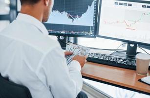 Calculating money. Young businessman in formal clothes is in office with multiple screens. Conception of exchange and money photo