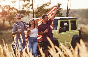 Friends have nice weekend outdoors near theirs green car with USA flag photo