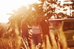 Giving cheers. Friends have nice weekend outdoors near theirs green car with USA flag photo