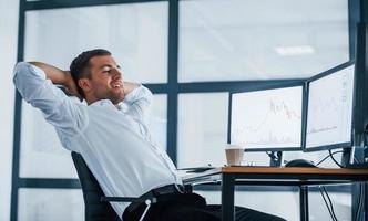 Taking a break. Young businessman in formal clothes is in office with multiple screens. Conception of exchange and money photo