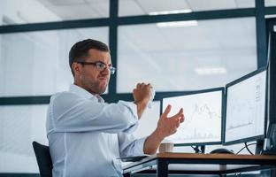 Angry employee throws paper. Conception of failure. Young businessman in formal clothes is in office with multiple screens photo